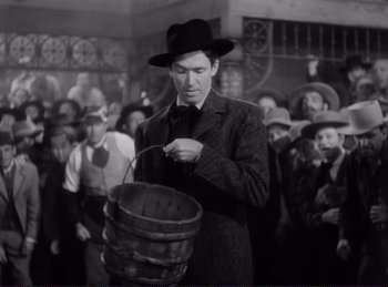 Movie still from “Destry Rides Again” (1939), directed by George Marshall – A man in a black hat holding a wooden bucket; Medium shot, Low angle