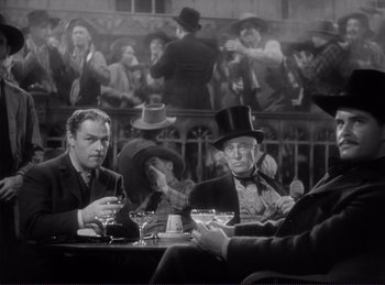 Movie still from “Destry Rides Again” (1939), directed by George Marshall – A group of men sitting at a table in front of a painting; Medium shot, Low angle
