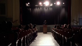 Movie still from “Detachment” (2011), directed by Tony Kaye – A man standing at a podium in front of an audience; Extreme Wide shot, High angle