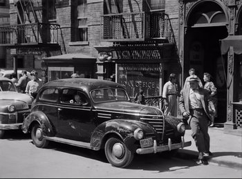Movie still from “Detective Story” (1951), directed by William Wyler – An old car parked on the side of the street; Wide shot, Low angle