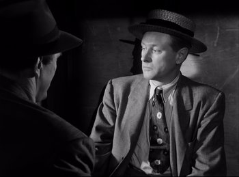 Movie still from “Detective Story” (1951), directed by William Wyler – A man in a suit and hat talking to another man in a hat; Medium shot, Over the shoulder angle