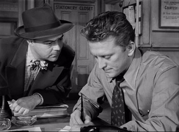 Movie still from “Detective Story” (1951), directed by William Wyler – A man in a hat and a man in a suit and tie; Medium shot, Over the shoulder angle