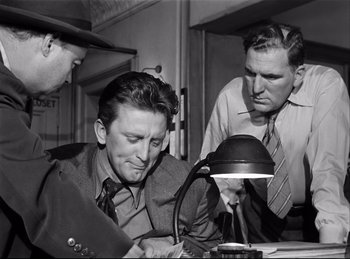 Movie still from “Detective Story” (1951), directed by William Wyler – A group of men standing around a table; Medium shot, Low angle