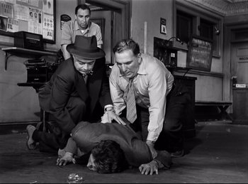 Movie still from “Detective Story” (1951), directed by William Wyler – A group of men standing around a man on the ground; Medium shot, Low angle