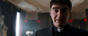 Movie still from “Detroit Rock City” (1999), directed by Adam Rifkin – A man wearing a priest's outfit in front of a building; Close Up shot, Low angle