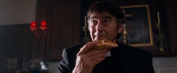 Movie still from “Detroit Rock City” (1999), directed by Adam Rifkin – A priest eating a piece of pizza in a room; Close Up shot, Low angle