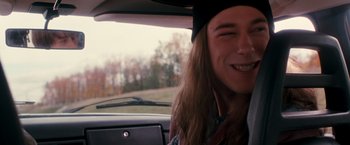 Movie still from “Detroit Rock City” (1999), directed by Adam Rifkin – A man with long hair is sitting in the back of a car; Close Up shot, High angle