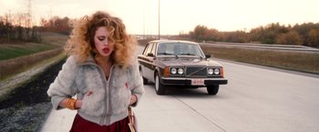 A woman walking down a street with a car in the background