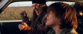 Movie still from “Detroit Rock City” (1999), directed by Adam Rifkin – Two young people laughing in a car on a road; Medium shot, High angle