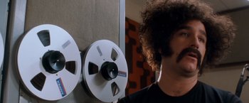 Movie still from “Detroit Rock City” (1999), directed by Adam Rifkin – A man standing in front of a wall with two reels of film; Close Up shot, Low angle