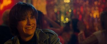 Movie still from “Detroit Rock City” (1999), directed by Adam Rifkin – A young man smiling for the camera in front of a christmas tree; Close Up shot, Over the shoulder angle