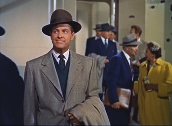 Movie still from “Dial M for Murder” (1954), directed by Alfred Hitchcock – A man in a suit and hat standing in front of a group of people; Medium shot, Low angle