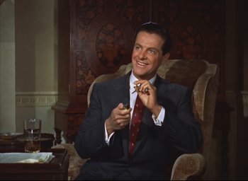Movie still from “Dial M for Murder” (1954), directed by Alfred Hitchcock – A man sitting in a chair holding a cigarette in his hand; Medium shot, Low angle