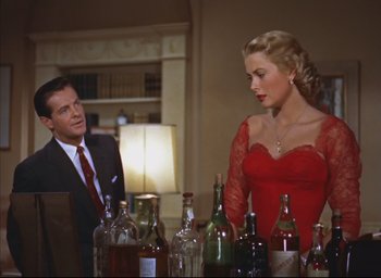 Movie still from “Dial M for Murder” (1954), directed by Alfred Hitchcock – A man and a woman in a red dress in front of many bottles; Medium shot, Over the shoulder angle