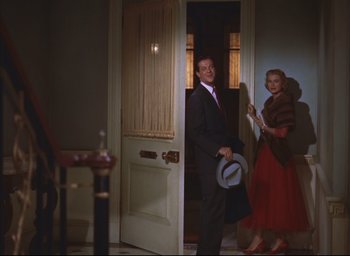 Movie still from “Dial M for Murder” (1954), directed by Alfred Hitchcock – A man and a woman are standing in the doorway of a house; Wide shot, Low angle