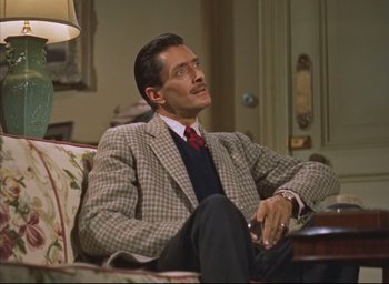 Movie still from “Dial M for Murder” (1954), directed by Alfred Hitchcock – A man sitting on top of a couch in a room; Medium shot, Low angle