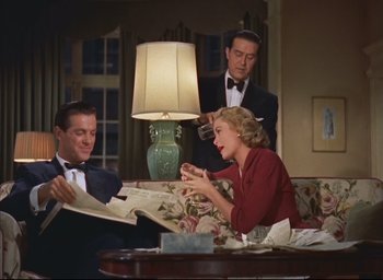 Movie still from “Dial M for Murder” (1954), directed by Alfred Hitchcock – A man and a woman sitting in front of another man holding papers; Medium shot, High angle