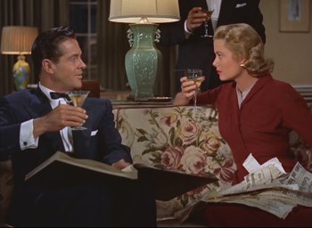 Movie still from “Dial M for Murder” (1954), directed by Alfred Hitchcock – A man and a woman sitting on a couch drinking wine; Medium shot, High angle