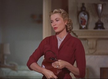 Movie still from “Dial M for Murder” (1954), directed by Alfred Hitchcock – A woman holding a brown purse while standing in a living room; Medium shot, Low angle