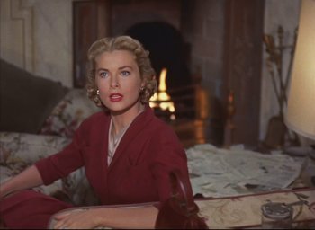 Movie still from “Dial M for Murder” (1954), directed by Alfred Hitchcock – A woman sitting on a couch in front of a fire place; Medium shot, Over the shoulder angle
