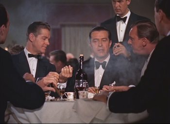 Movie still from “Dial M for Murder” (1954), directed by Alfred Hitchcock – A group of men sitting at a table with drinks; Medium shot, Over the shoulder angle
