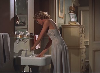 Movie still from “Dial M for Murder” (1954), directed by Alfred Hitchcock – A woman in a white dress standing in front of a bathroom sink; Medium shot, Low angle