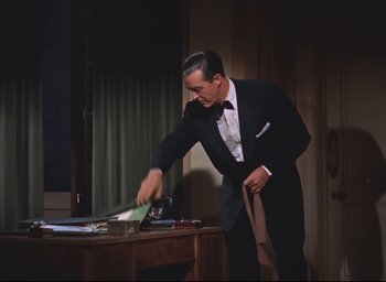 Movie still from “Dial M for Murder” (1954), directed by Alfred Hitchcock – A man in a suit and bow tie cutting paper; Medium shot, Low angle