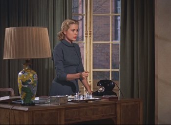Movie still from “Dial M for Murder” (1954), directed by Alfred Hitchcock – A woman standing in front of a desk with a phone; Medium shot, Low angle