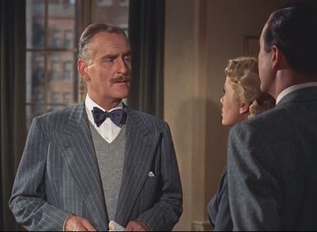 Movie still from “Dial M for Murder” (1954), directed by Alfred Hitchcock – An older man wearing a suit and bow tie talking to two other people; Medium shot, Low angle