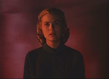 Movie still from “Dial M for Murder” (1954), directed by Alfred Hitchcock – A woman with blonde ringlets in front of a red background; Close Up shot, Low angle