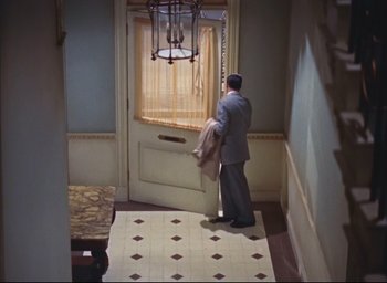 Movie still from “Dial M for Murder” (1954), directed by Alfred Hitchcock – A man standing in front of a door in a room; Wide shot, High angle