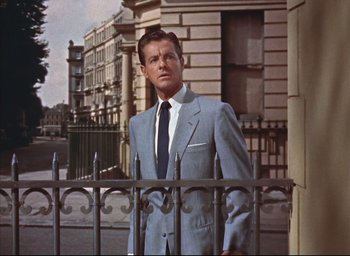 Movie still from “Dial M for Murder” (1954), directed by Alfred Hitchcock – A man wearing a suit and tie standing next to a fence; Medium shot, Low angle
