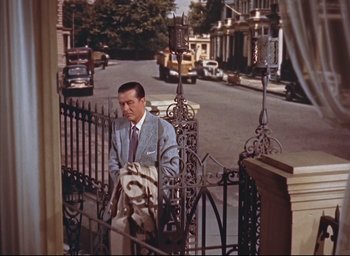 Movie still from “Dial M for Murder” (1954), directed by Alfred Hitchcock – A man in a suit and tie sitting on a fence; Wide shot, Low angle