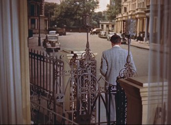 Movie still from “Dial M for Murder” (1954), directed by Alfred Hitchcock – A man standing on the side of the road near a gate; Wide shot, High angle