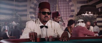 Movie still from “Diamonds Are Forever” (1971), directed by Guy Hamilton – A man sitting at a poker table wearing a fez; Medium shot, Low angle
