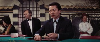 Movie still from “Diamonds Are Forever” (1971), directed by Guy Hamilton – A man sitting at a table in front of cards; Medium shot, Over the shoulder angle