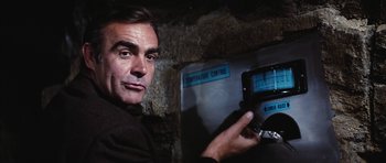 Movie still from “Diamonds Are Forever” (1971), directed by Guy Hamilton – A man is holding an electronic device in front of a wall; Close Up shot, Low angle