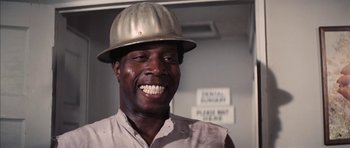 Movie still from “Diamonds Are Forever” (1971), directed by Guy Hamilton – A man wearing a hard hat smiles for the camera; Close Up shot, Low angle