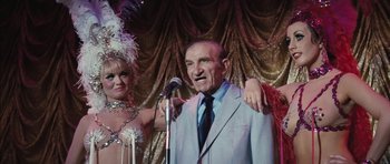 Movie still from “Diamonds Are Forever” (1971), directed by Guy Hamilton – An older man wearing a suit and tie with a microphone; Medium shot, Low angle