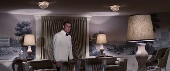 Movie still from “Diamonds Are Forever” (1971), directed by Guy Hamilton – A man in a white suit standing in a living room; Wide shot, Low angle