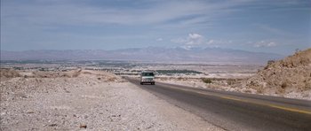 Movie still from “Diamonds Are Forever” (1971), directed by Guy Hamilton – A car driving down a desert road with mountains in the background; Extreme Wide shot, High angle