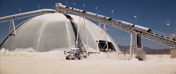 Movie still from “Diamonds Are Forever” (1971), directed by Guy Hamilton – A truck driving down a dirt road next to a conveyor belt; Extreme Wide shot, High angle