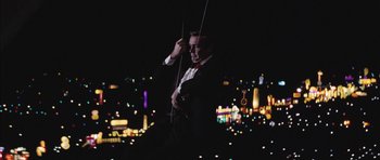 Movie still from “Diamonds Are Forever” (1971), directed by Guy Hamilton – A man in a suit and tie holding a violin; Wide shot, Low angle