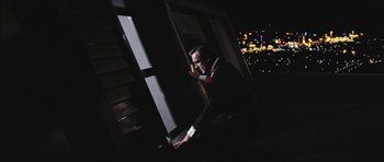 Movie still from “Diamonds Are Forever” (1971), directed by Guy Hamilton – A man sitting at a desk in front of a window at night; Medium shot, Low angle