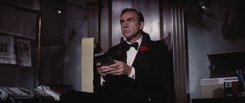 Movie still from “Diamonds Are Forever” (1971), directed by Guy Hamilton – A man in a tuxedo holding a cell phone in his hands; Medium shot, Low angle