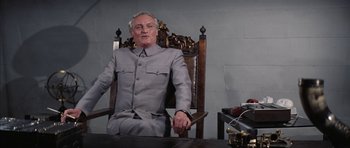 Movie still from “Diamonds Are Forever” (1971), directed by Guy Hamilton – An older man sitting in a chair holding a knife in his hand; Medium shot, Low angle