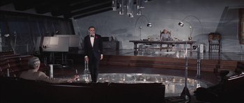 Movie still from “Diamonds Are Forever” (1971), directed by Guy Hamilton – A man in a tuxedo standing in front of a dining room table; Wide shot, Low angle