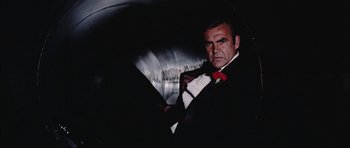 Movie still from “Diamonds Are Forever” (1971), directed by Guy Hamilton – A man in a tuxedo standing in a dark room; Medium shot, Low angle