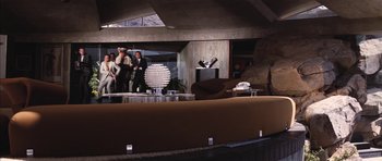 Movie still from “Diamonds Are Forever” (1971), directed by Guy Hamilton – A group of people standing in a room with furniture; Extreme Wide shot, Low angle