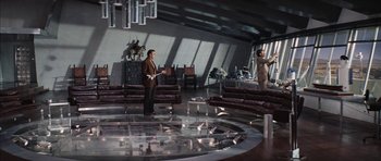 Movie still from “Diamonds Are Forever” (1971), directed by Guy Hamilton – A man standing in front of another man in a living room; Wide shot, High angle